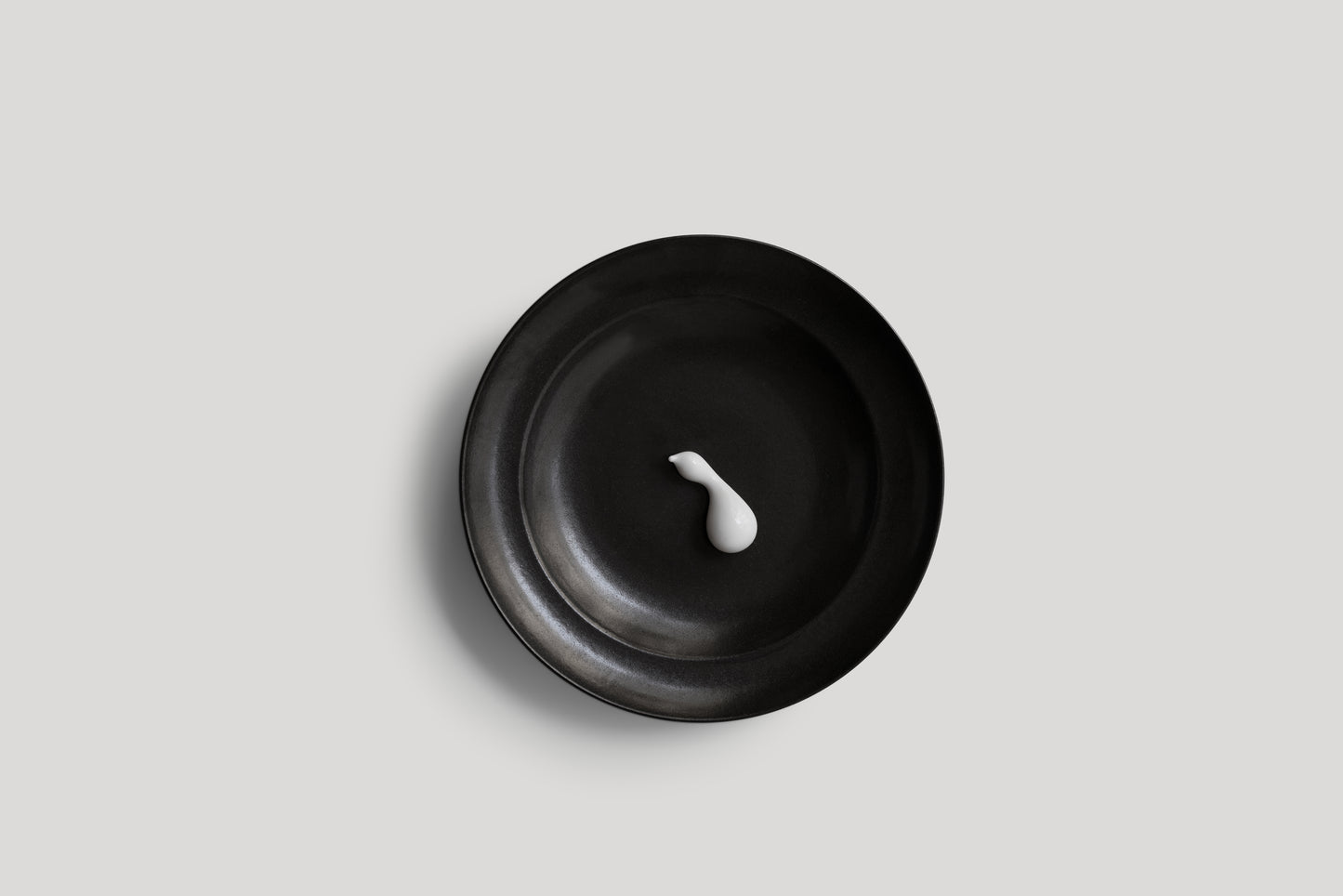 Black bowl with a white candle on a light gray background