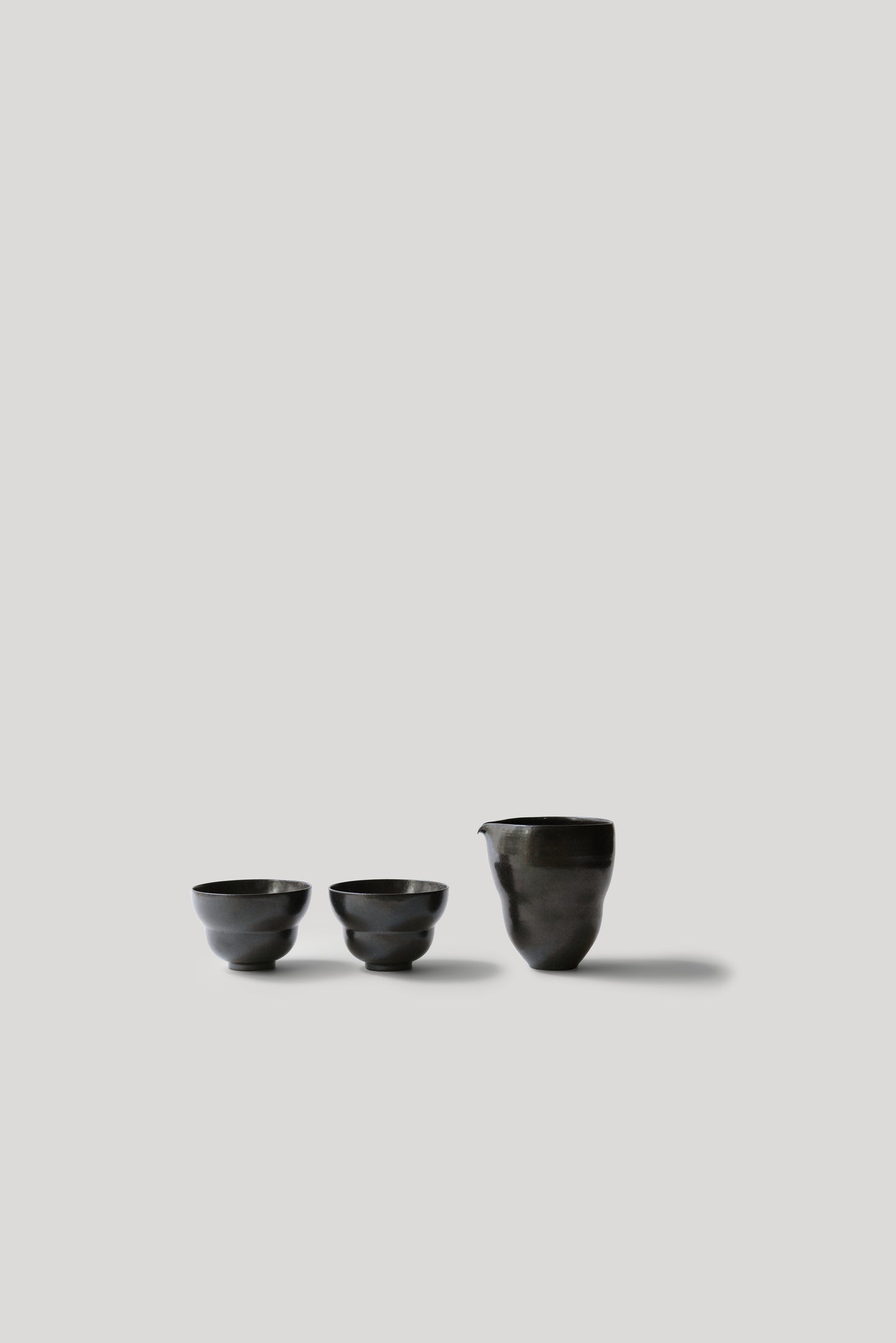 Three black ceramic cups of varying sizes on a light gray background