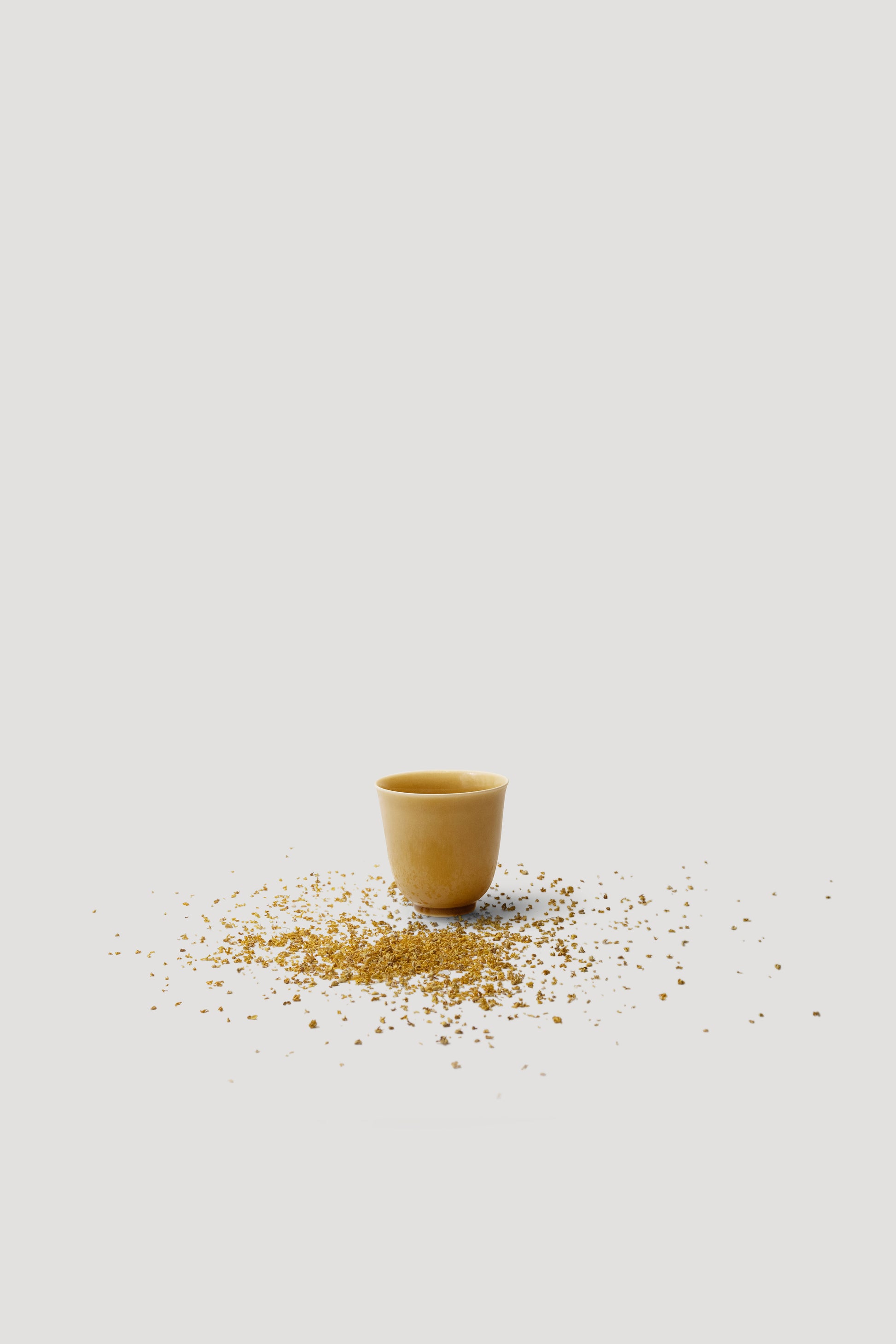 Small yellow cup with scattered seeds on a light gray background