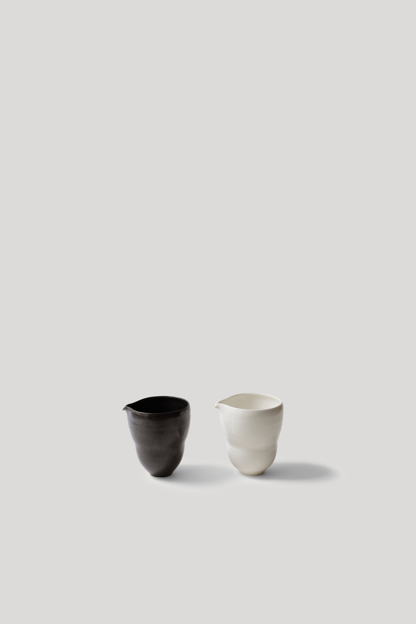 Two ceramic cups, one black and one white, on a light gray background