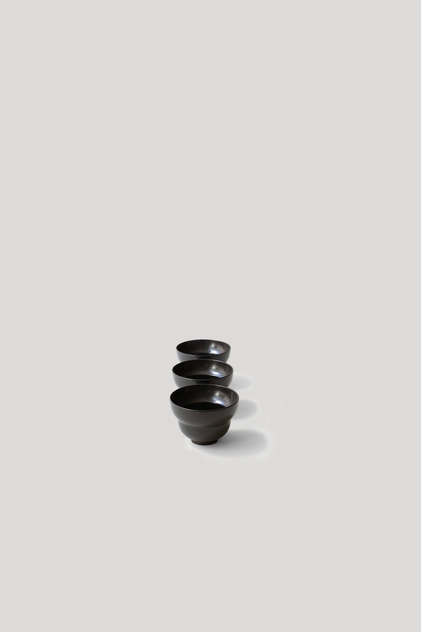 Three black ceramic cups on a light gray background