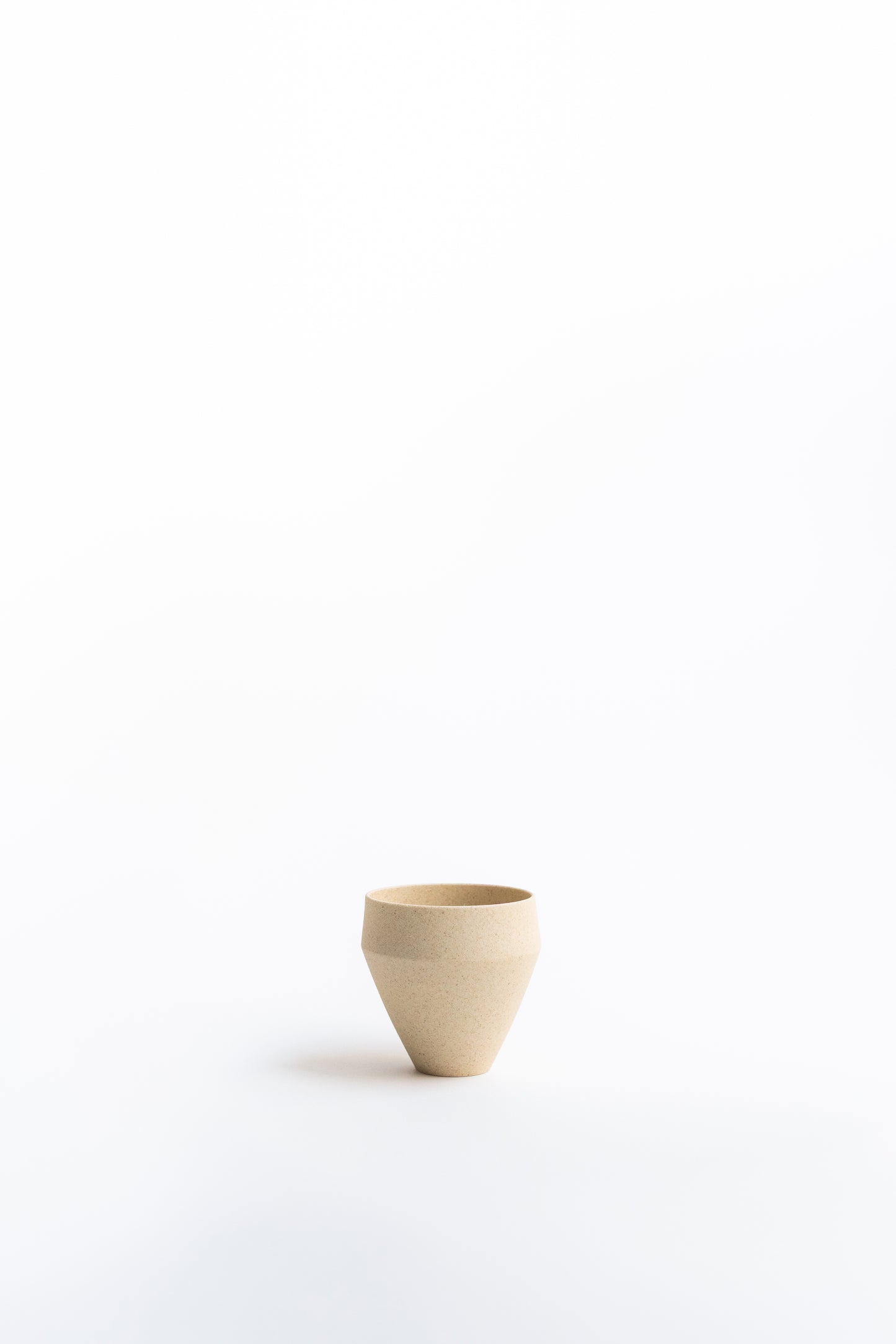 Small beige ceramic cup on a white background