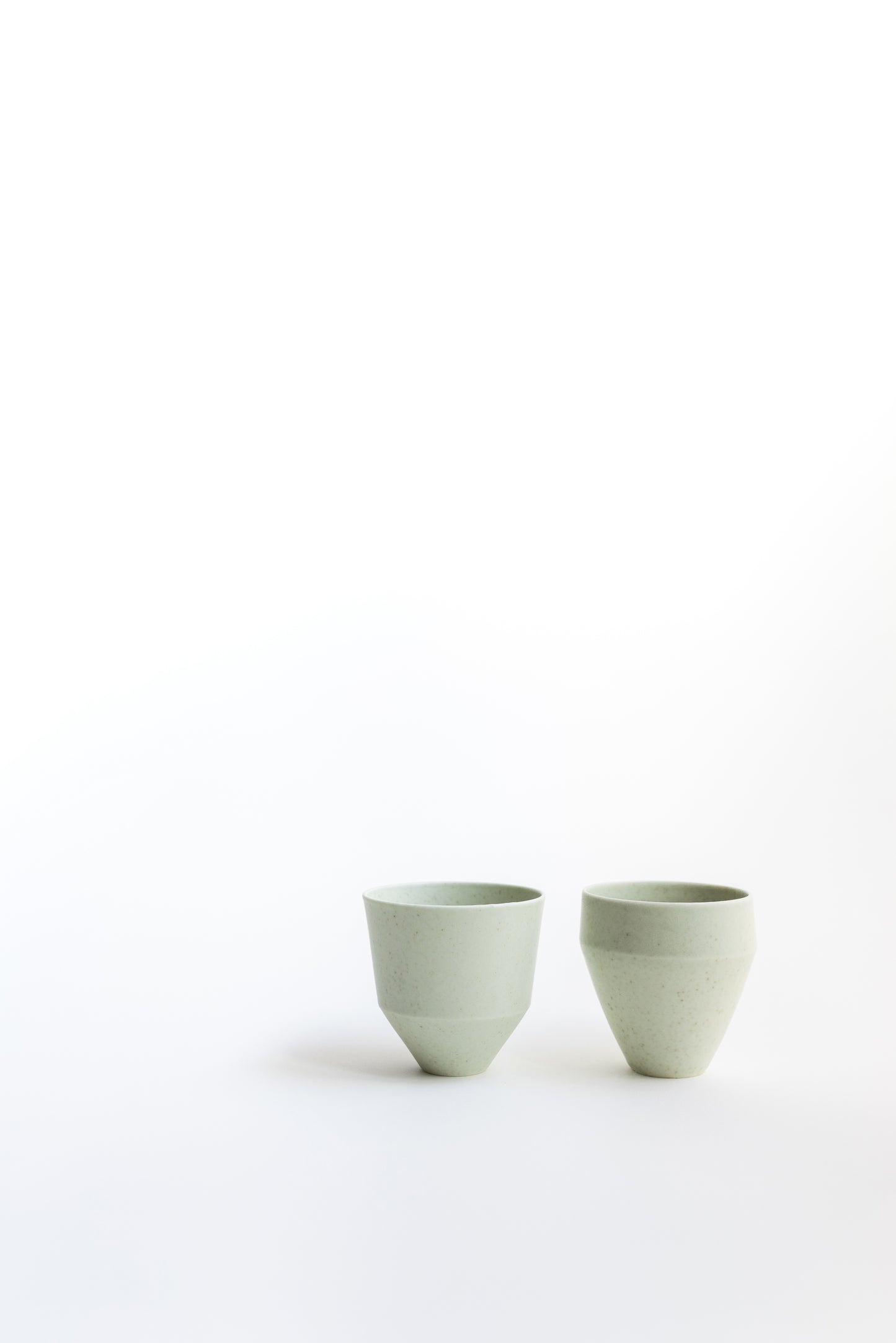 Two light green ceramic cups on a white background