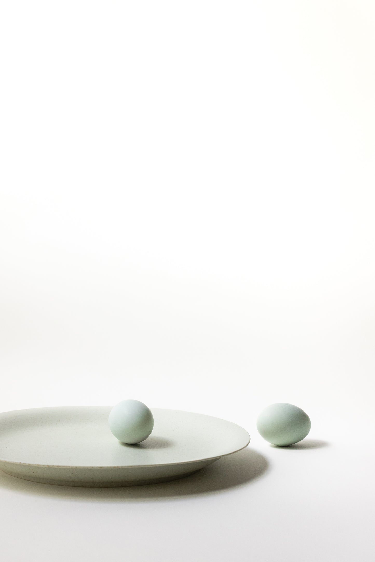 Two light green ceramic balls on a white plate against a white background