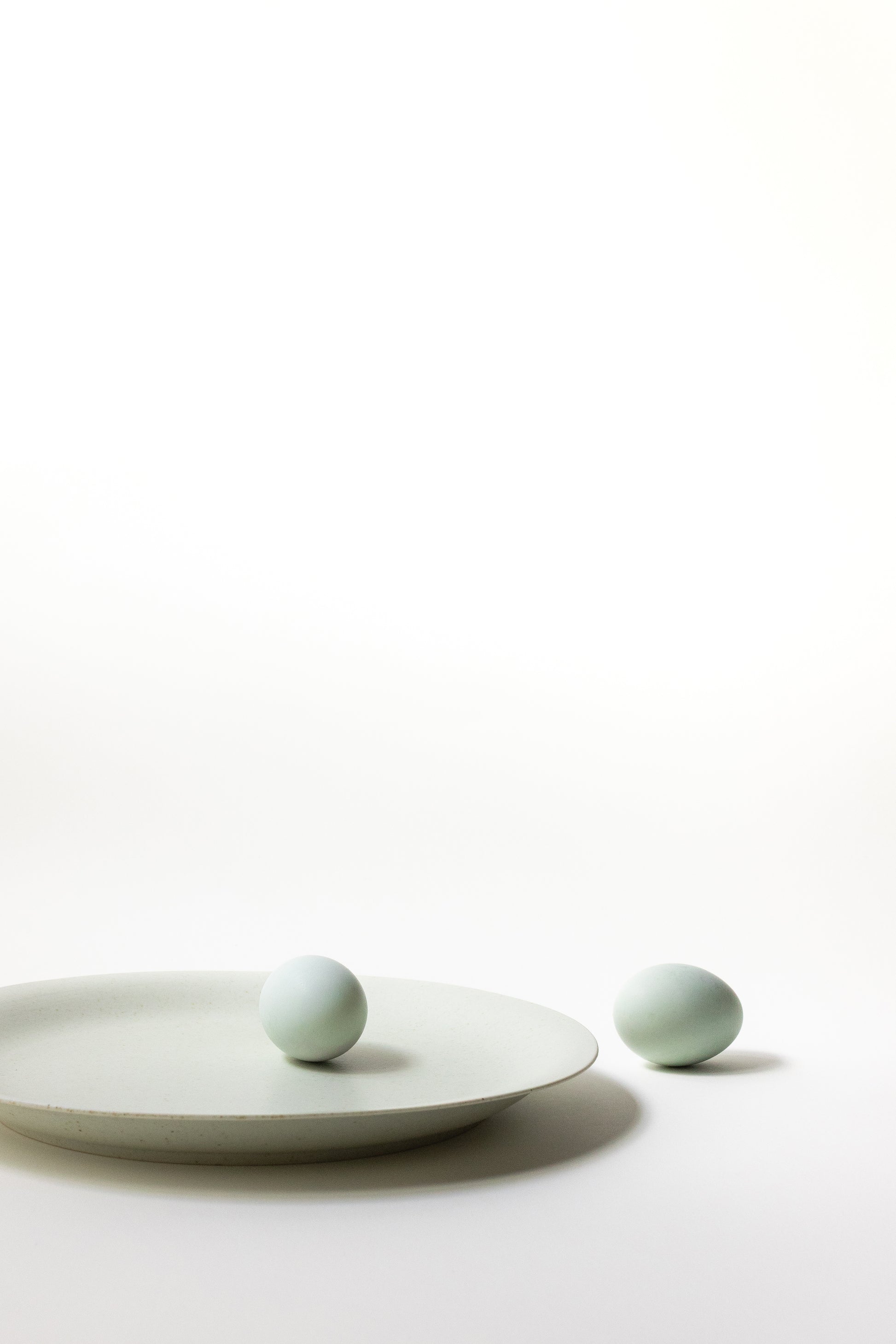 Two light green ceramic balls on a white plate against a white background