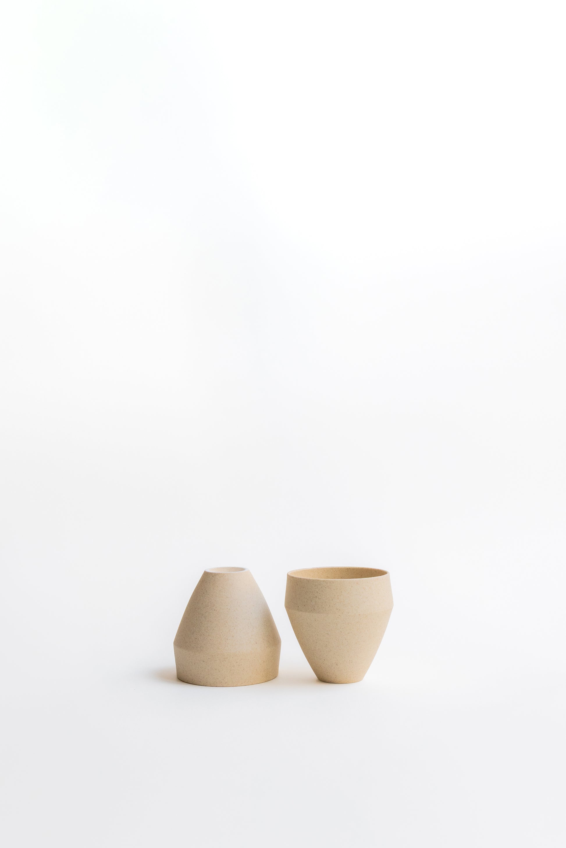Two small beige ceramic cups on a white background