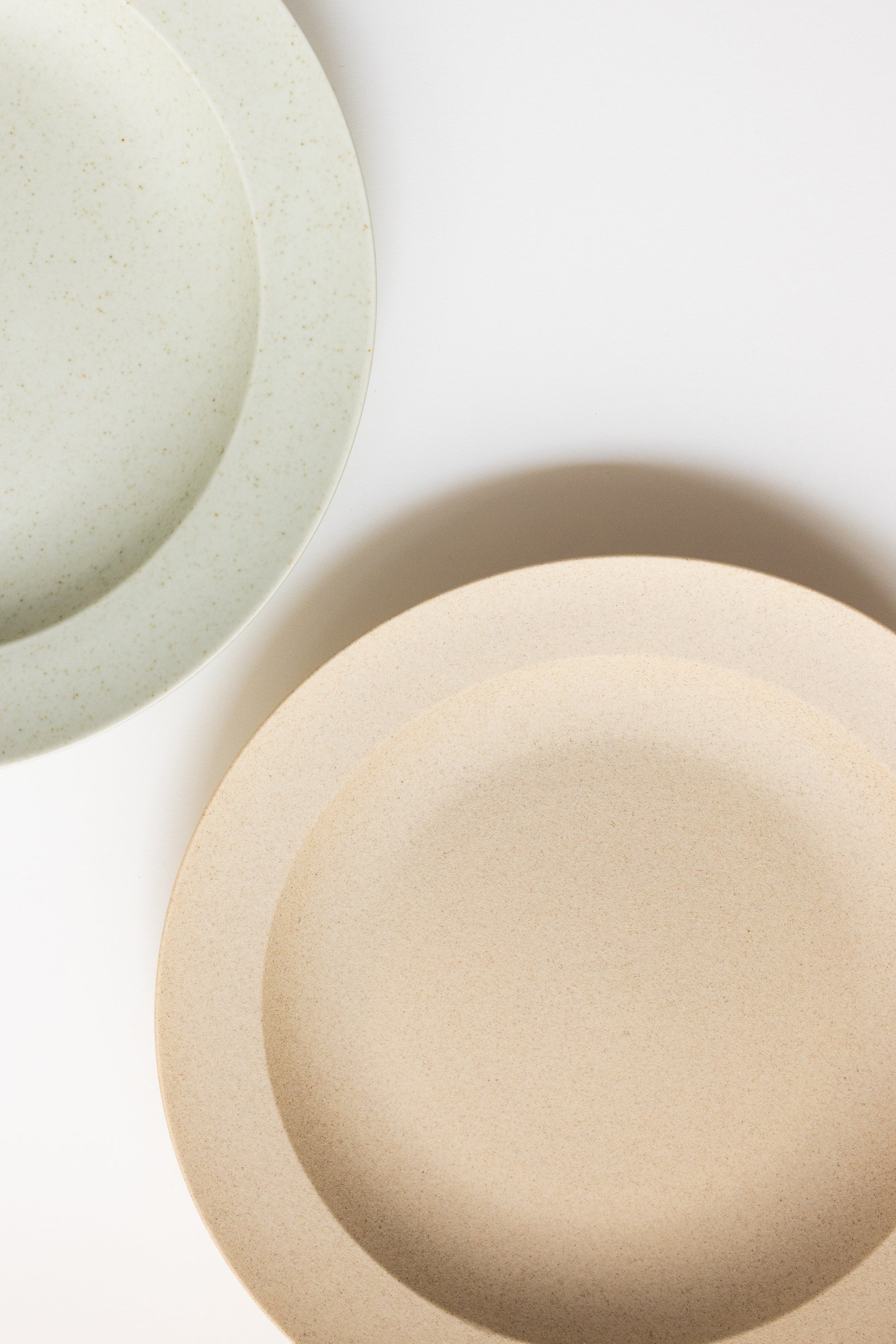 Two ceramic bowls, one beige and one light green, on a white background