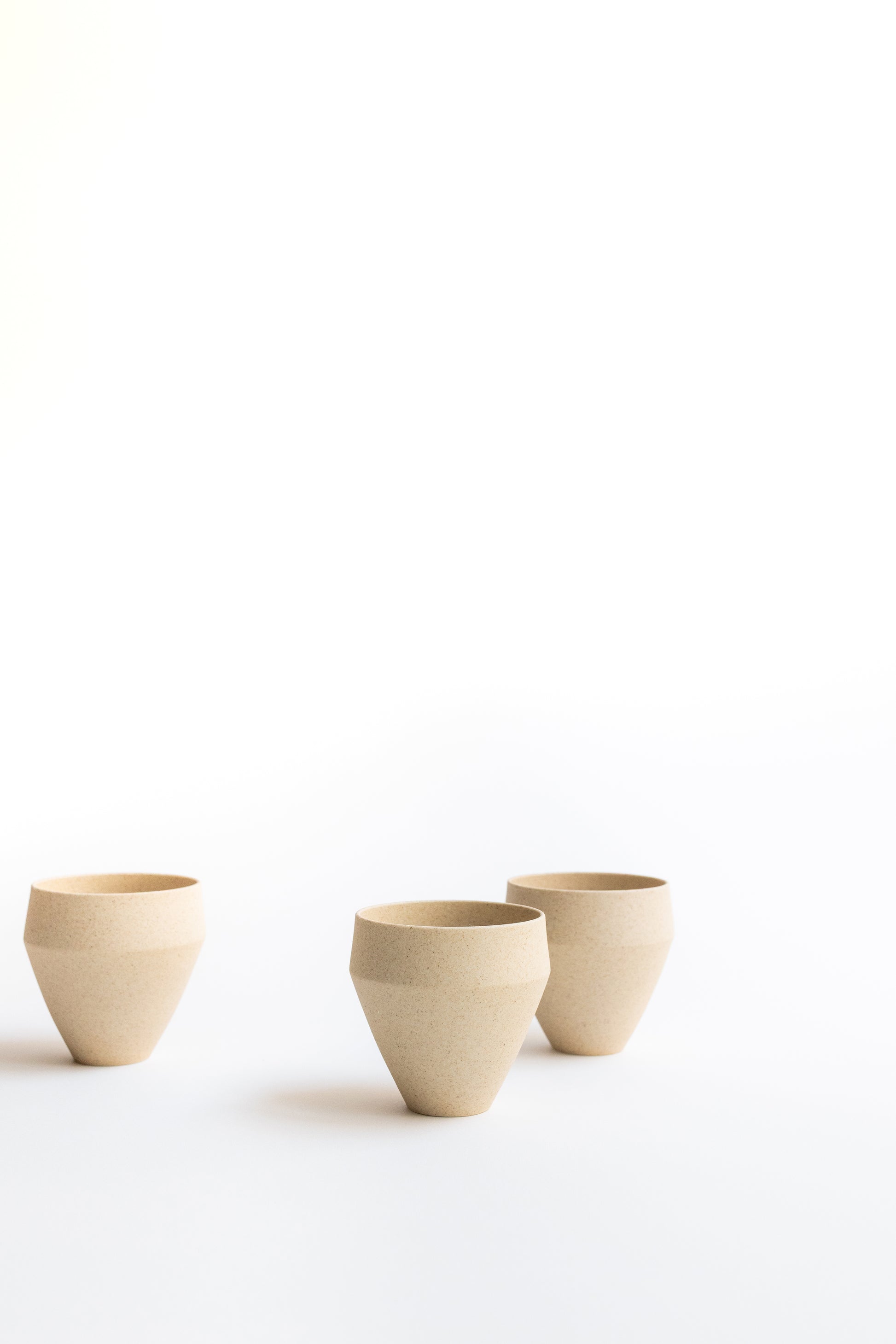 Three beige ceramic cups on a white background