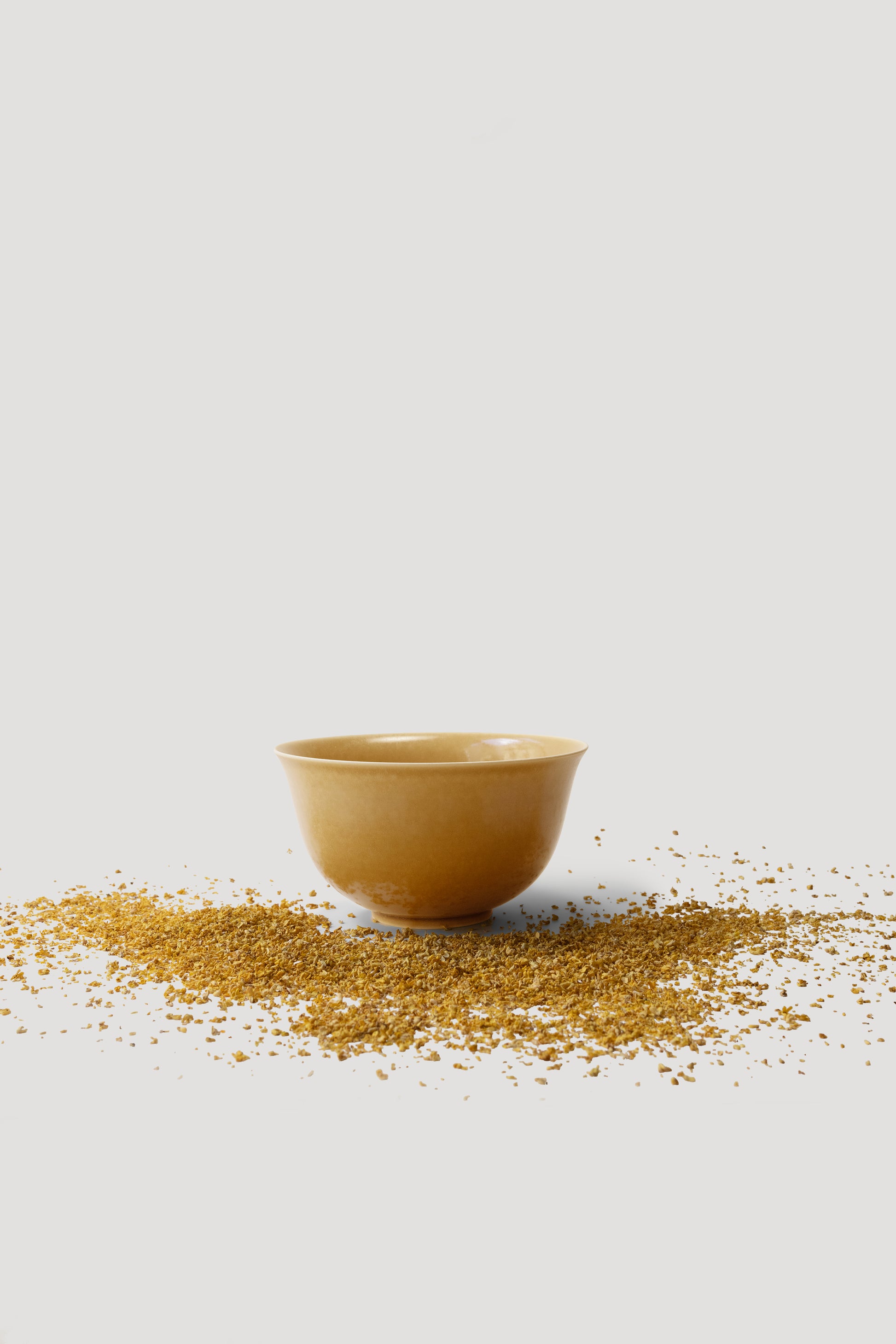 Yellow ceramic bowl with scattered grain on a light gray background