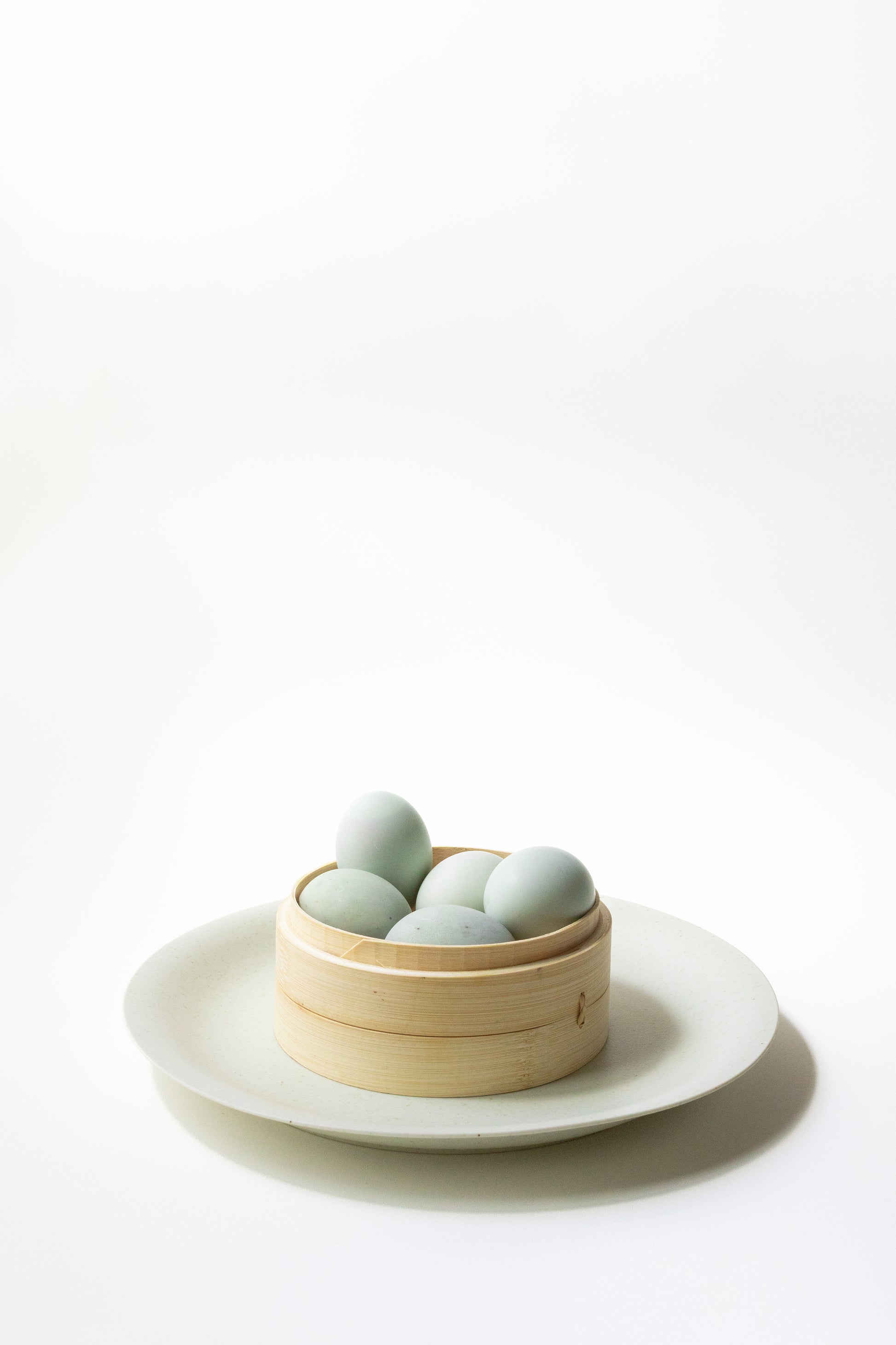 Bamboo basket with light green eggs on a white plate against a white background